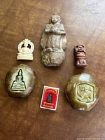 Top view of the six figurines including two polished oval stones with carved images, a seated figure, two smaller figurines, and a red boxed amulet image.