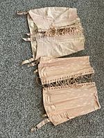 Photo of two antique lace-up corsets laid flat on the ground displaying the outer side, showing attached garter straps and fabric texture.