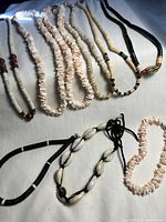 Top view of assorted puka shell and BoHo style necklaces and anklets arranged on flat surface showing varied bead styles and materials.
