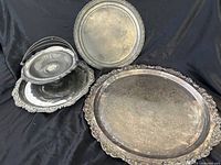 Three pieces of silver servingware: two large round platters and a round handled basket, all showing tarnish.