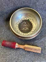 Top view showing the interior embossed Buddha medallion and lotus flower design inside the antique Tibetan singing bowl, alongside the wooden mallet.