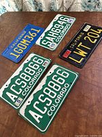 Overview of all five vintage license plates displayed on a table: three Colorado plates and two California plates, showing condition and embossed details.