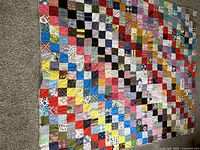 Full view of large patchwork quilt spread on carpet, showing its colorful square fabric patches in multiple patterns and colors.