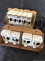 Two sets of vintage ceramic salt, pepper, and spice shakers with rooster designs mounted on wooden racks, arranged on black background.