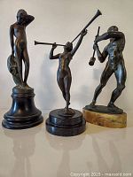 Three bronze statues arranged side by side on a flat surface against a white background