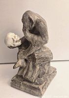 Front right angle of the Darwin thinker stone sculpture showing the monkey holding a skull above books with visible 'DARWIN' etching on the spine.