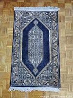 Full view of rug laid flat on parquet floor showing overall design, color and fringes.