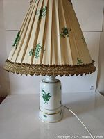 Front view of lamp showing porcelain base and pleated shade with green floral design and brown/gold trim.