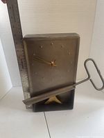 Front view showing metal clock face, dot markers, hands, ruler for scale, and detached metal support