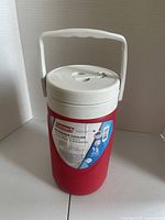 Front view showing red body, label, white lid, handle