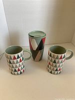 Front view of travel mug and two handled mugs showing geometric pattern