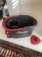 Side view of Vileda black and red spin mop bucket, separate red triangular mop head attachment visible