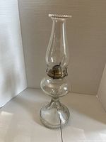 Full view of clear glass oil lamp showing base, font, burner, and chimney