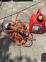 Work light with metal cage and cord alongside 5 L red gas can