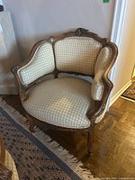 Front angle showing carved wood frame and beige upholstered seat and backrest of the chair.