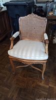 Front view of one carved wood chair showing cane back, carved crest and striped seat cushion