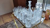 Full set of crystal decanters and glasses arranged on a brass and glass cart; includes two decanters and multiple glasses of various styles.