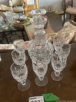 Full lot showing one crystal decanter with stopper and seven small Waterford glasses arranged around it on a wooden table.
