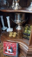 Two silver-plated ice buckets, white ceramic candle holders, yellow candles, festive napkins displayed on wooden shelves.