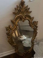 Front angled view of the ornate gold-toned mirror showing intricate carved frame details and clear reflection.