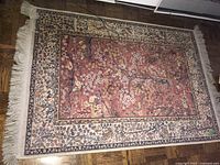Full view of rug on hardwood floor, showing central rose pink field, borders and fringe.