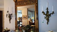 Two metal wall candle sconces flanking a mirror. Each holds three taper candles. Gilt finish with ornate scroll design.