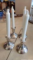 Four sterling silver weighted candle holders on a table with white taper candles inserted, showing overall set and scale.