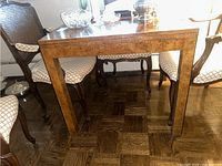 Wood square table shown from a front angle with adjacent chairs and crystal items on top.