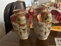 Two porcelain vases side by side showing detailed hand-painted scenic and floral designs with gold highlights.