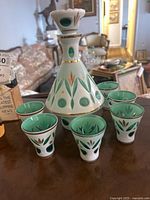 The whole decanter set including the decanter and six matching cups on a table with a vintage room background.