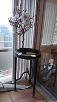 Faux magnolia plant on plant stand by window, showing full height and details of flowers and leaves.
