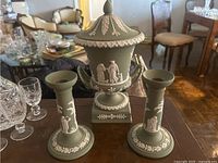 Front view of sage green jasperware urn with lid flanked by two matching candlesticks on wooden table
