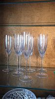 Eight clear Wedgwood champagne glasses arranged on a glass shelf.