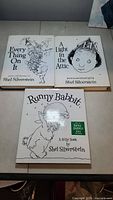 Top view of three hardcover books by Shel Silverstein arranged on a beige surface: Every Thing On It, A Light in the Attic, Runny Babbit.