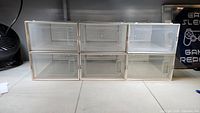 Front view of six stackable transparent plastic shoe boxes arranged in two rows of three, showing front doors and ventilation holes.