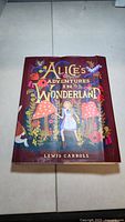 Front cover of the paperback book Alice's Adventures in Wonderland, showing a colorful design with Alice, mushrooms, and floral elements.