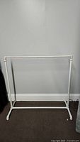 Full view of white clothes rack made of metal pipes against a light gray wall
