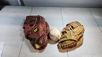 Two baseball gloves and one baseball on a white surface