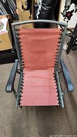 Front view of folding patio chair showing reddish fabric and grey metal frame with armrests.