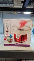 Front view of the product box showing the Nostalgia Hard Candy Cotton Candy Maker with a cotton candy swirl and colorful candy pieces in bowls.
