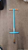 Blue pogo stick laying on a carpeted floor, showing orange foam handles and black rubber foot tip.