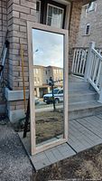 Photo of full-length standing mirror outdoors, showing wooden frame and clear reflective surface.