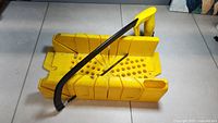 Yellow plastic Stanley deluxe miter box with multiple slots and holes for angled cutting and clamping. Black metal hacksaw frame with yellow handle placed inside the box.