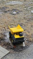 Yellow Tonka dump truck toy placed outdoors on dirt ground, showing front and top view.