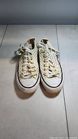 Front view of pair of women's Converse sneakers, white with gold polka dots, laced and showing rubber toe cap and sole.