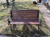 Front view of outdoor wood bench with cast iron frame showing seat and backrest horizontal wooden slats and black cast iron armrests and legs