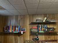 Wide view of multiple shelves on a wood-paneled wall holding assorted novels and some decorative items.