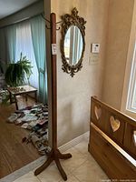 Full view of wooden coat rack standing on tile floor, showing the vertical post and angled four-legged base near a wooden bench and wall.