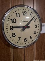 Front view of the Ingraham wall clock showing cream dial and black numbers with red second hand.
