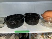 Three black speckled roasting pans with lids and clear glass casserole dish on shelf.